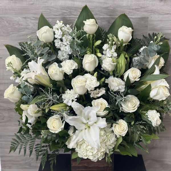 White roses and lilies arranged in a wooden box with greenery.
