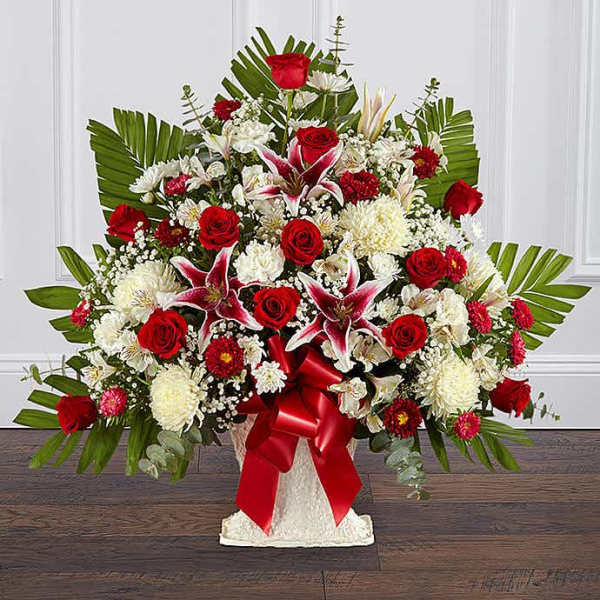 Large red and white flower arrangement with lilies and roses in a white urn with red ribbon