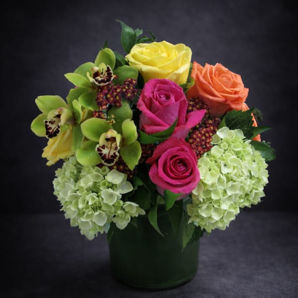 Colorful bouquet of roses, orchids, and hydrangeas in a dark vase