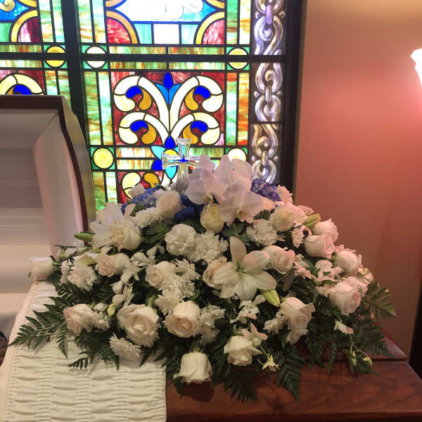 White floral casket spray with a cross in a church setting