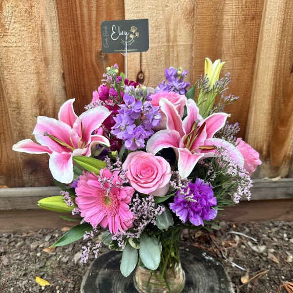 Pink lilies, roses, and purple flowers in a glass vase