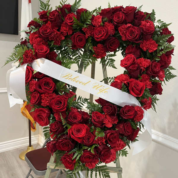 Heart-shaped red rose wreath with a white ribbon reading "Beloved Wife"