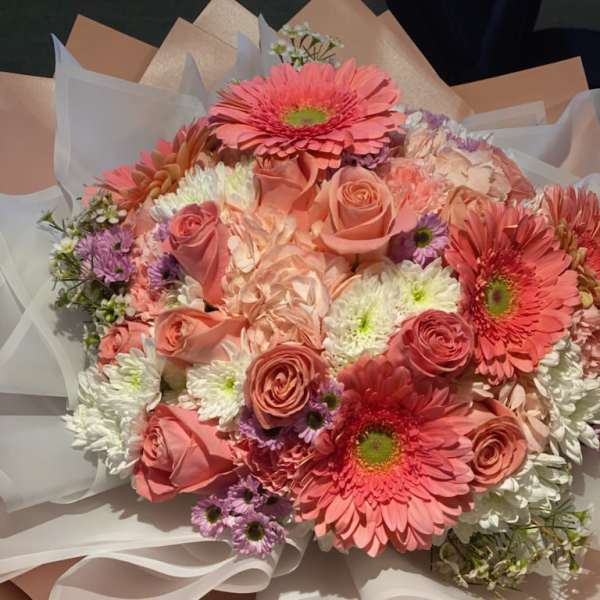 Bouquet of pink gerbera daisies, roses, and white chrysanthemums wrapped in paper