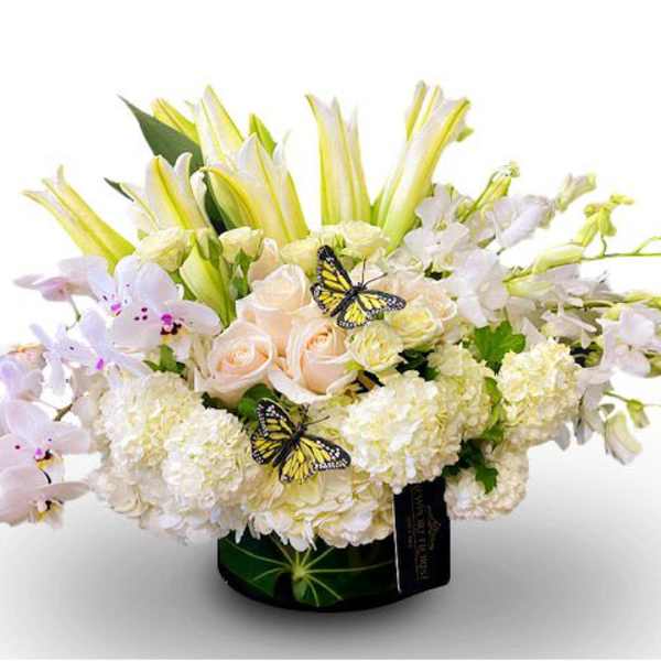 White and pale pink floral arrangement in a black vase with butterfly accents