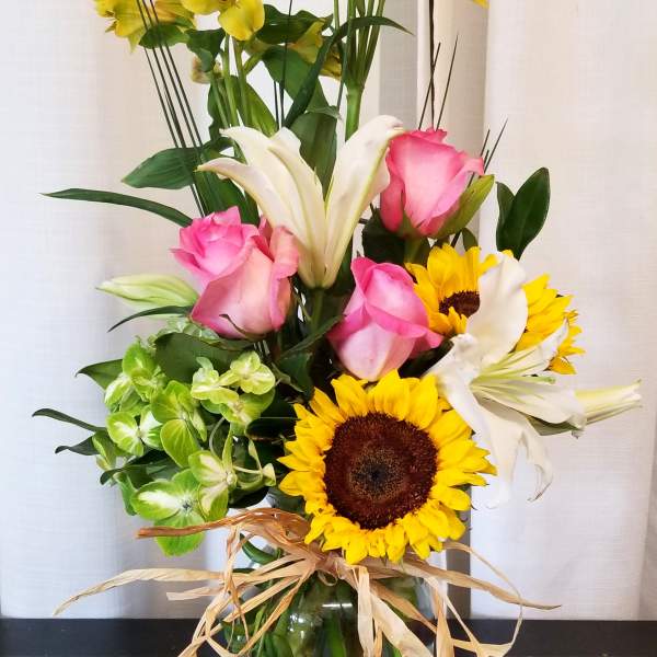 Mixed bouquet with pink roses, sunflowers, white lilies, and yellow alstroemeria in a glass vase