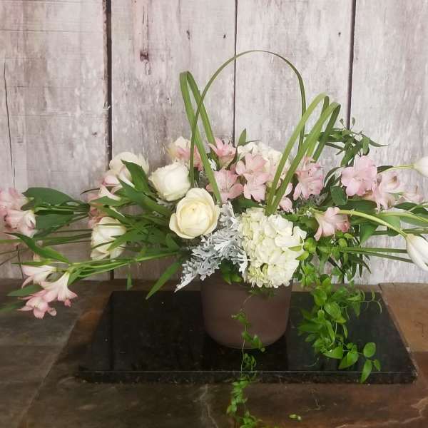 Low floral arrangement with white roses, pink blooms, and long white tulips in a brown pot