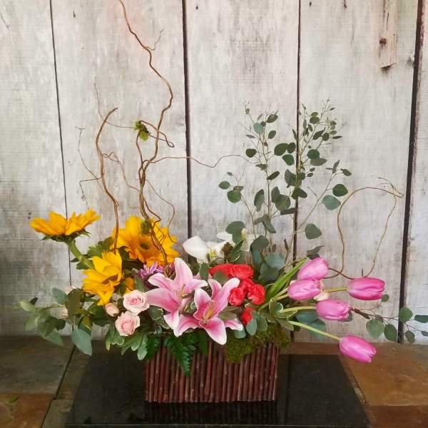 Mixed floral arrangement with sunflowers, lilies, roses, and pink tulips in a rectangular container