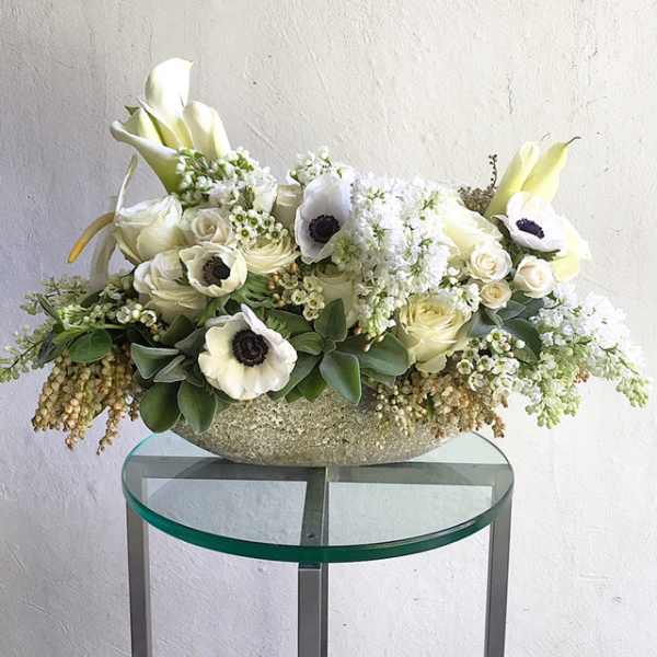 White floral arrangement in a textured bowl on a glass table