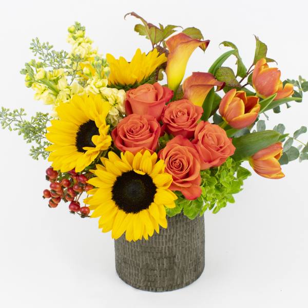 Bouquet of sunflowers, orange roses, and orange tulips in a textured vase
