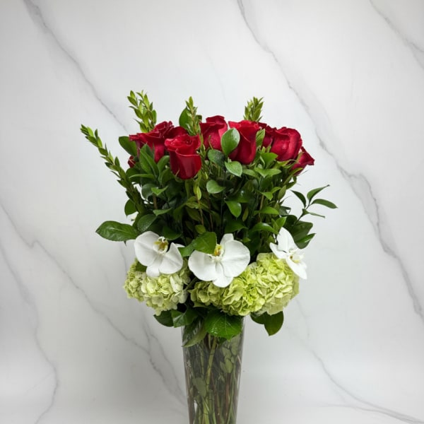 Red roses and white orchids arranged in a tall glass vase