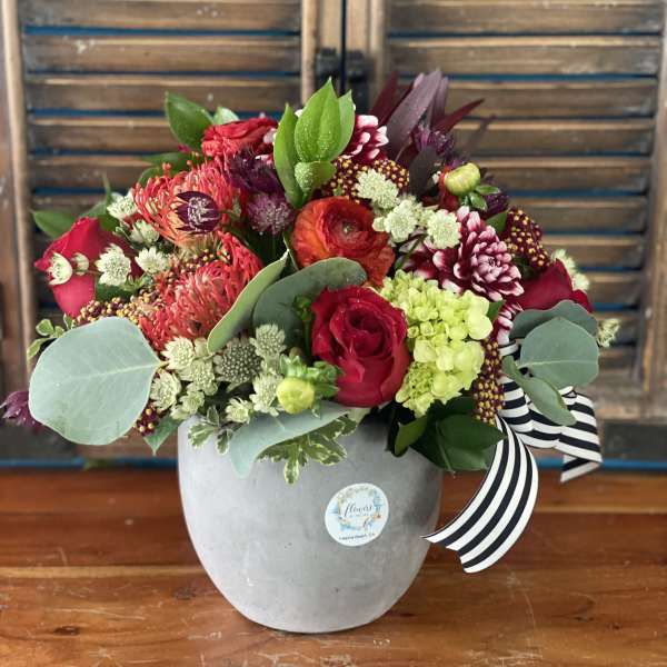 Mixed red and pink flower arrangement in a gray vase with a striped ribbon