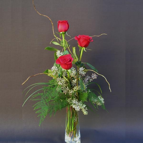 Tall vase arrangement with three red roses and white filler flowers