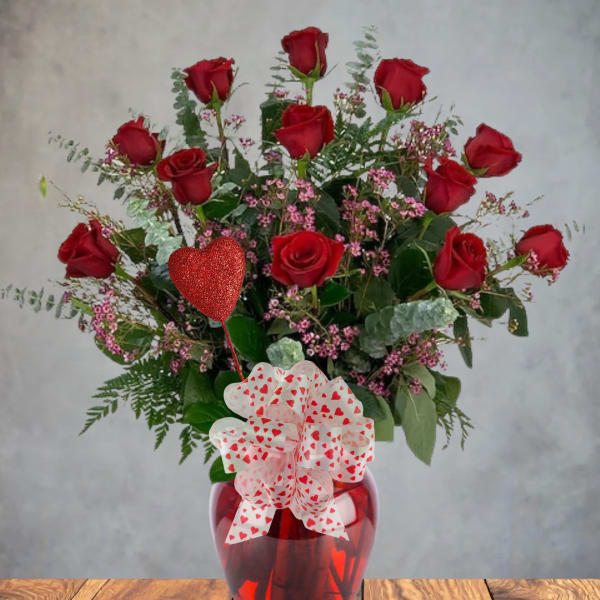 Red roses in a red glass vase with a heart-patterned bow and balloon