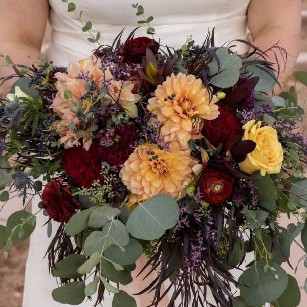 Bride holding a bouquet of peach, red, and yellow flowers with eucalyptus