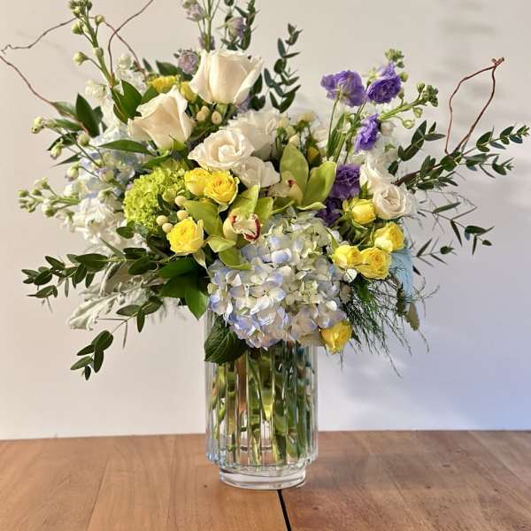 Mixed bouquet of white, yellow, purple, and blue flowers in a glass vase
