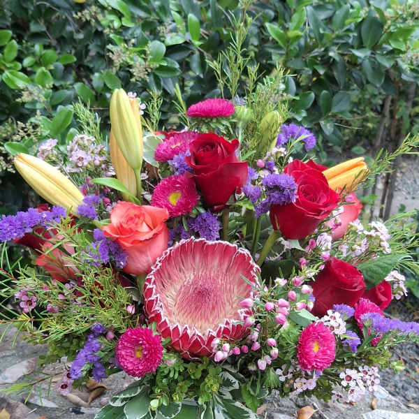 Mixed bouquet with red roses, lilies, and a protea in a striped vase