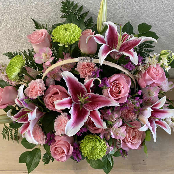 Pink roses and lilies arranged in a basket with green mums