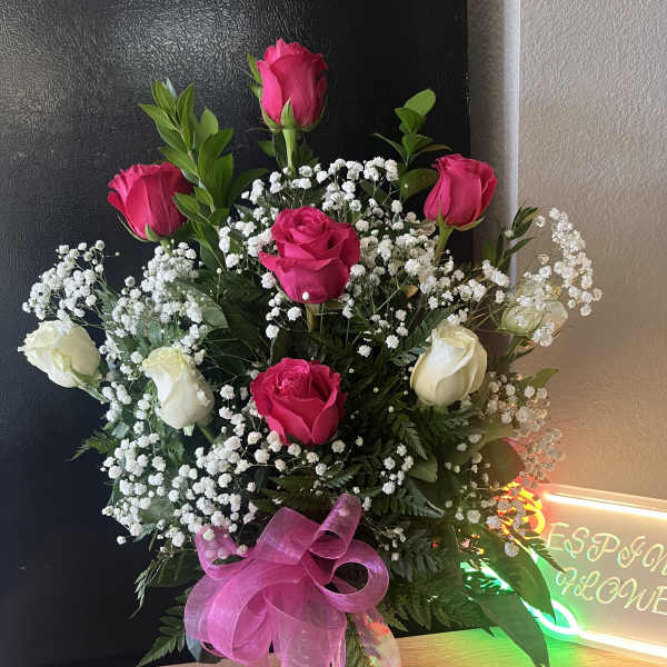 Tall vase arrangement of hot pink and white roses with baby's breath and a pink bow in a clear glass vase