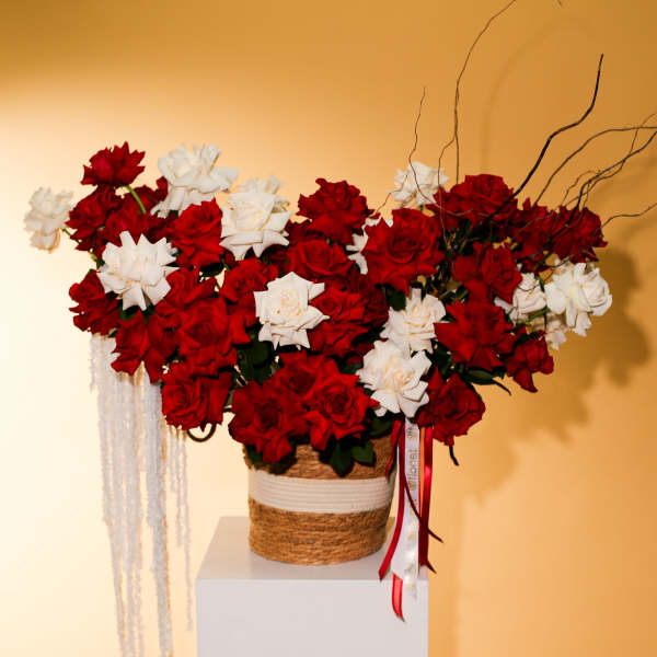 Red and white roses arranged in a woven basket with ribbon accents