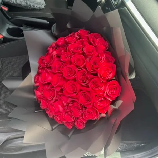 Large bouquet of red roses wrapped in black paper on a car seat