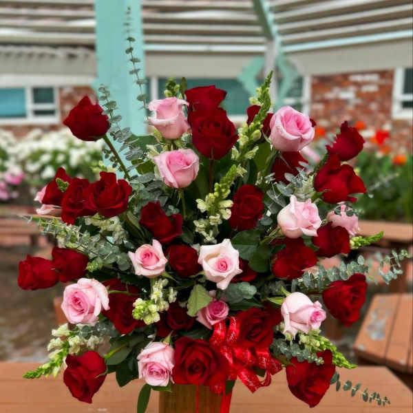 Red and pink roses arranged in a tall vase with ribbon