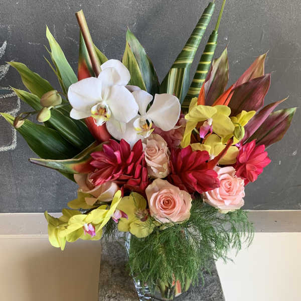 Tropical bouquet with orchids, roses, and red blooms in a glass vase