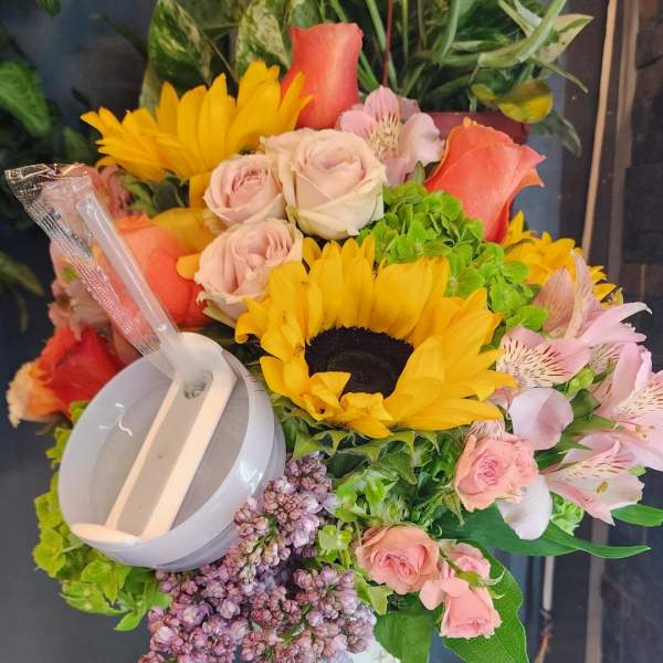 Bright mixed bouquet with sunflowers and roses arranged in a tall patterned travel mug with lid and straw.