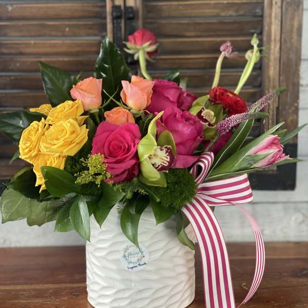 Colorful rose arrangement in a white ceramic vase with a striped ribbon