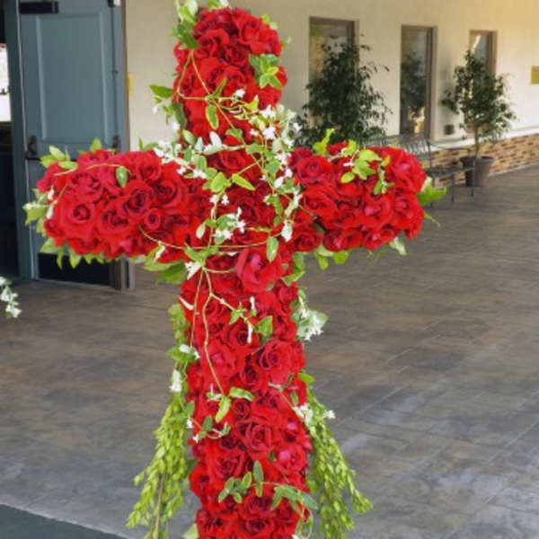 Large cross-shaped arrangement of red roses with trailing greenery