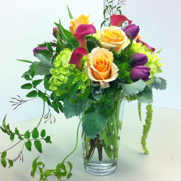 Bouquet of orange roses, purple tulips, and green hydrangeas in a glass vase