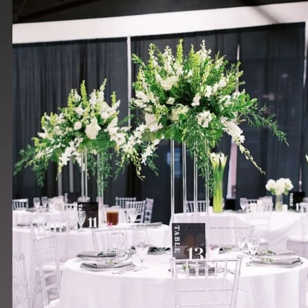 Tall white floral centerpieces on clear stands at round banquet tables