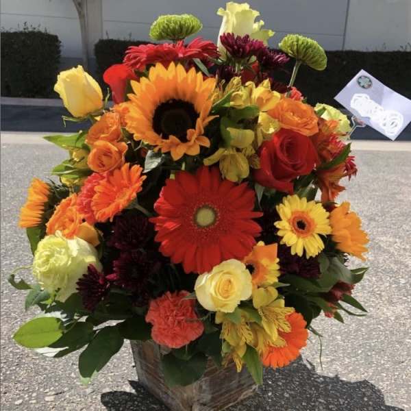 Bright mixed bouquet with sunflowers, roses, and gerbera daisies in a square vase