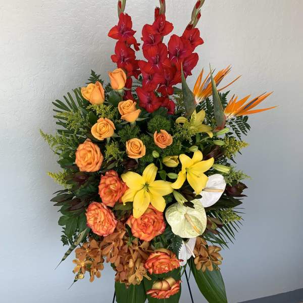 Tall tropical flower arrangement with red gladiolus, orange roses, yellow lilies, and white anthuriums