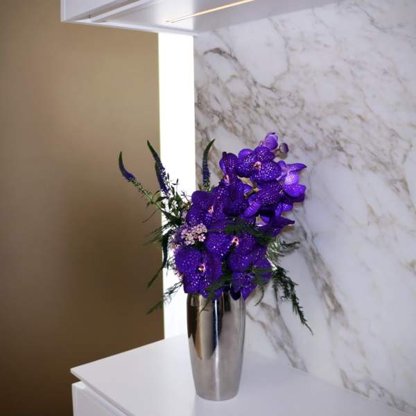 Purple orchids arranged in a tall silver vase