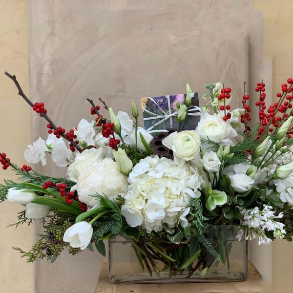 White floral arrangement with red berry branches in a glass vase