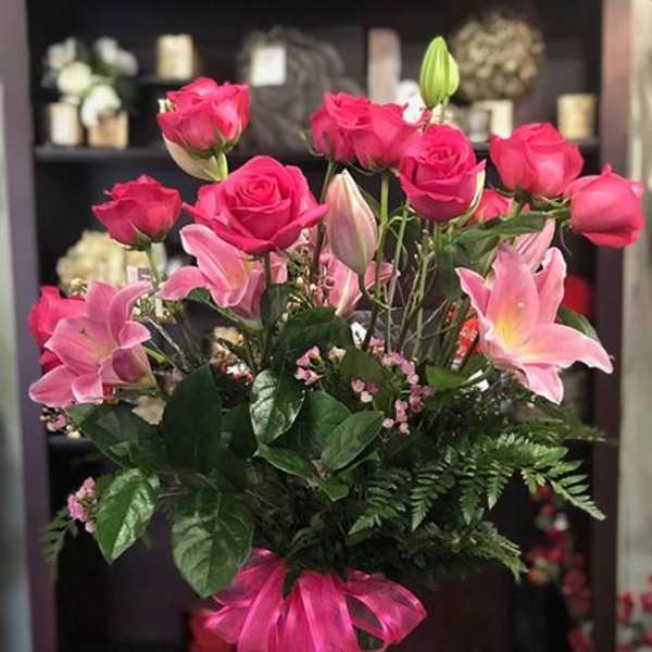 Pink roses and lilies arranged in a glass vase with a pink ribbon