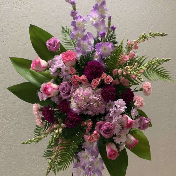 Standing floral spray with pink and purple flowers on a black easel