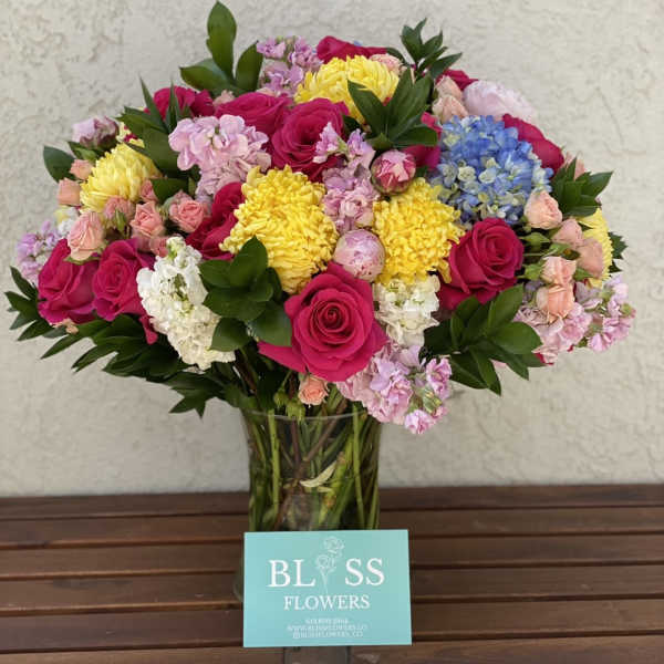 Mixed bouquet of roses, hydrangeas, and yellow blooms in a glass vase