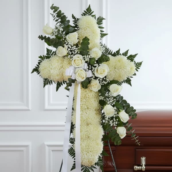 White floral funeral cross on an easel beside a casket