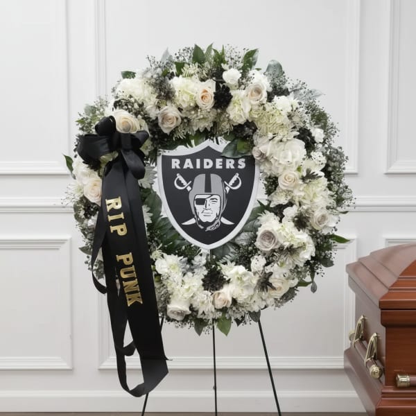 White floral funeral wreath with a Raiders emblem and black ribbon