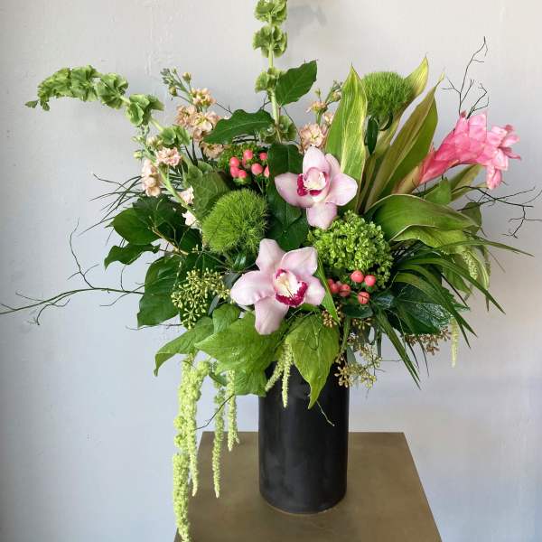 Tall floral arrangement with pink orchids in a black vase