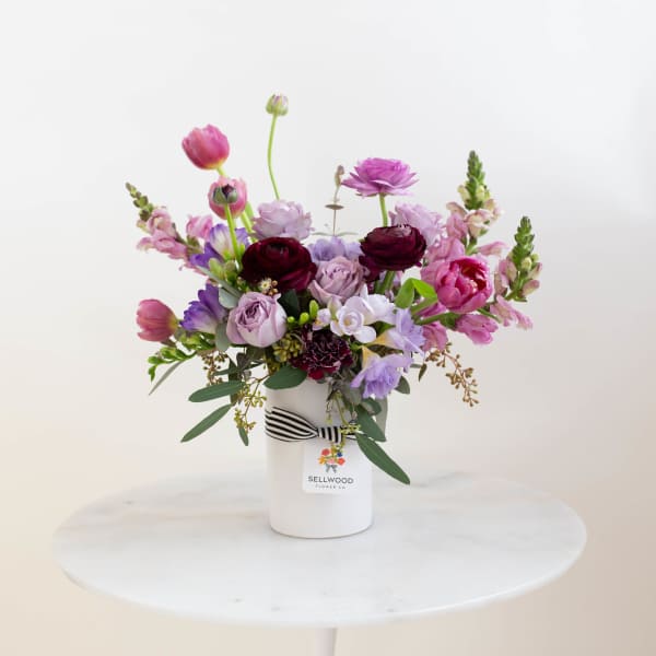 Mixed pink and purple bouquet in a white vase with a striped ribbon