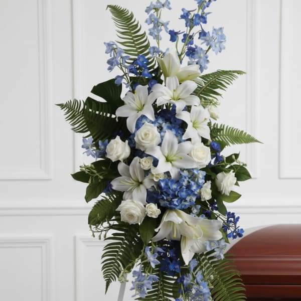 White lilies and blue flowers arranged on a funeral easel beside a casket