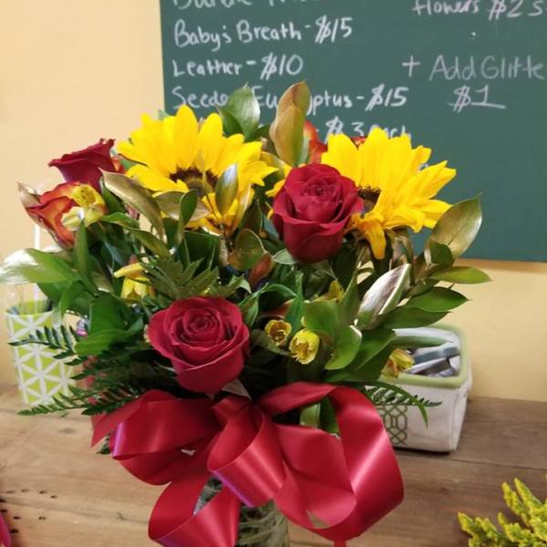 Bouquet of red roses and yellow sunflowers in a glass vase with a red ribbon