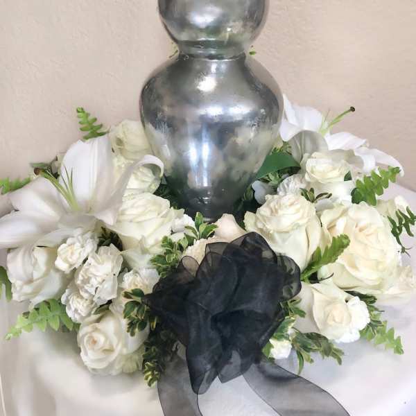 White rose arrangement around a silver urn with a black ribbon