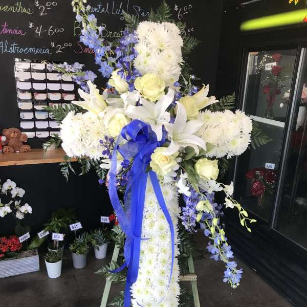 White floral standing cross with blue ribbon and yellow roses