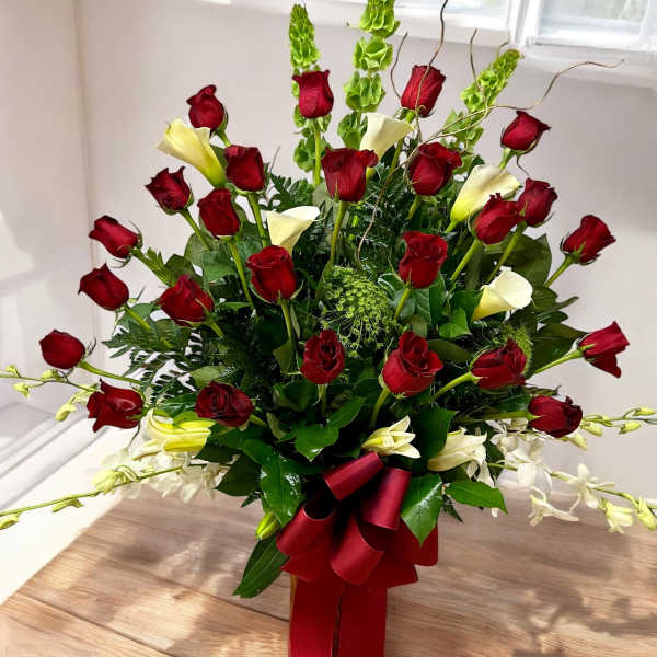 Tall arrangement of red roses, white calla lilies, and green bells of Ireland with a red bow.
