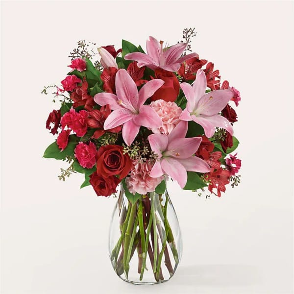 Arrangement of pink lilies, red roses, and pink carnations in a clear glass vase
