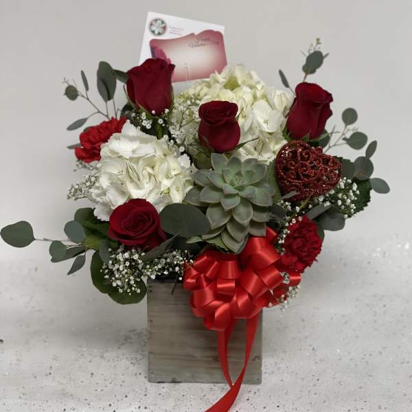 Red roses and white hydrangeas in a wooden box with a red ribbon.