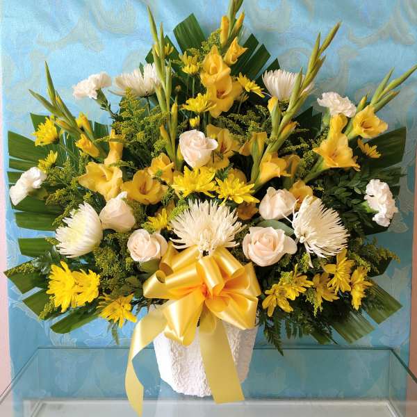 Yellow and white floral arrangement in a white vase with a yellow ribbon